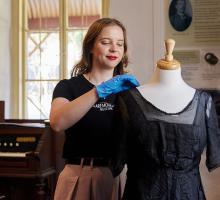 Staff member at Claremont Museum pinning a dress to a dress-making mannequin