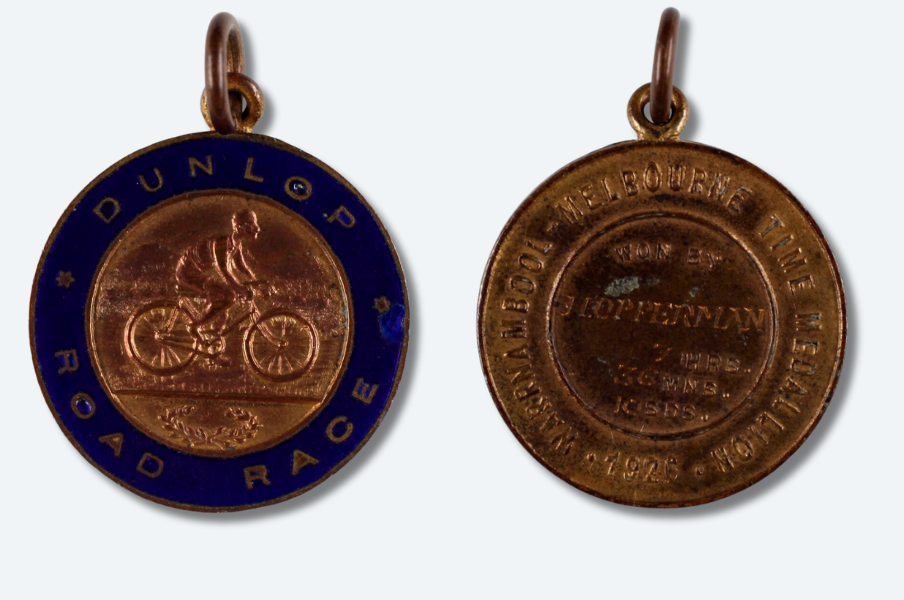 The Dunlop Road Race medal. The front side has an image of a person riding a bike etched into the medal. The back side of the Dunlop Road Race medal. It says 1926 Melbourne Times Medallion and is awarded to H. Opperman.