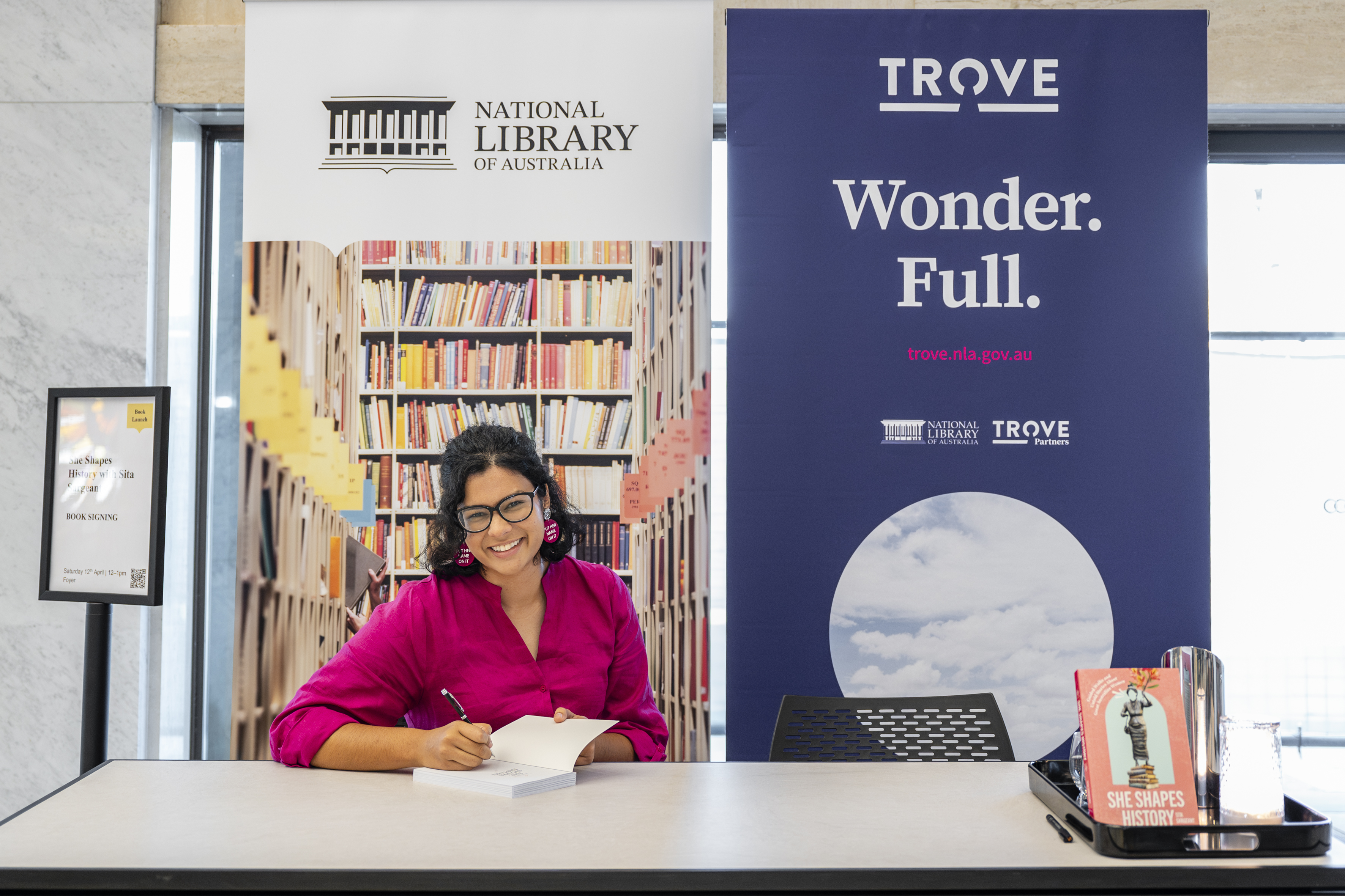 Sita signing her book at the National Library next to a Trove banner