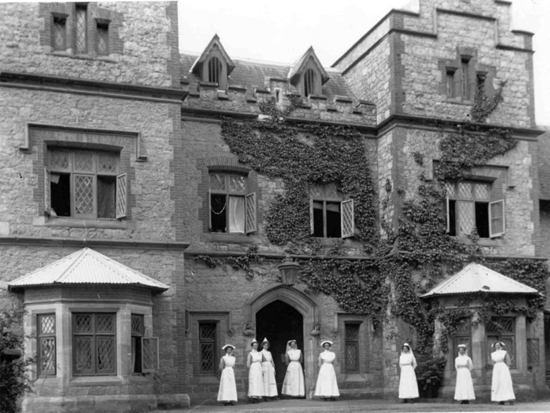 A large building with vines growing up one side and nurses standing in front of it.