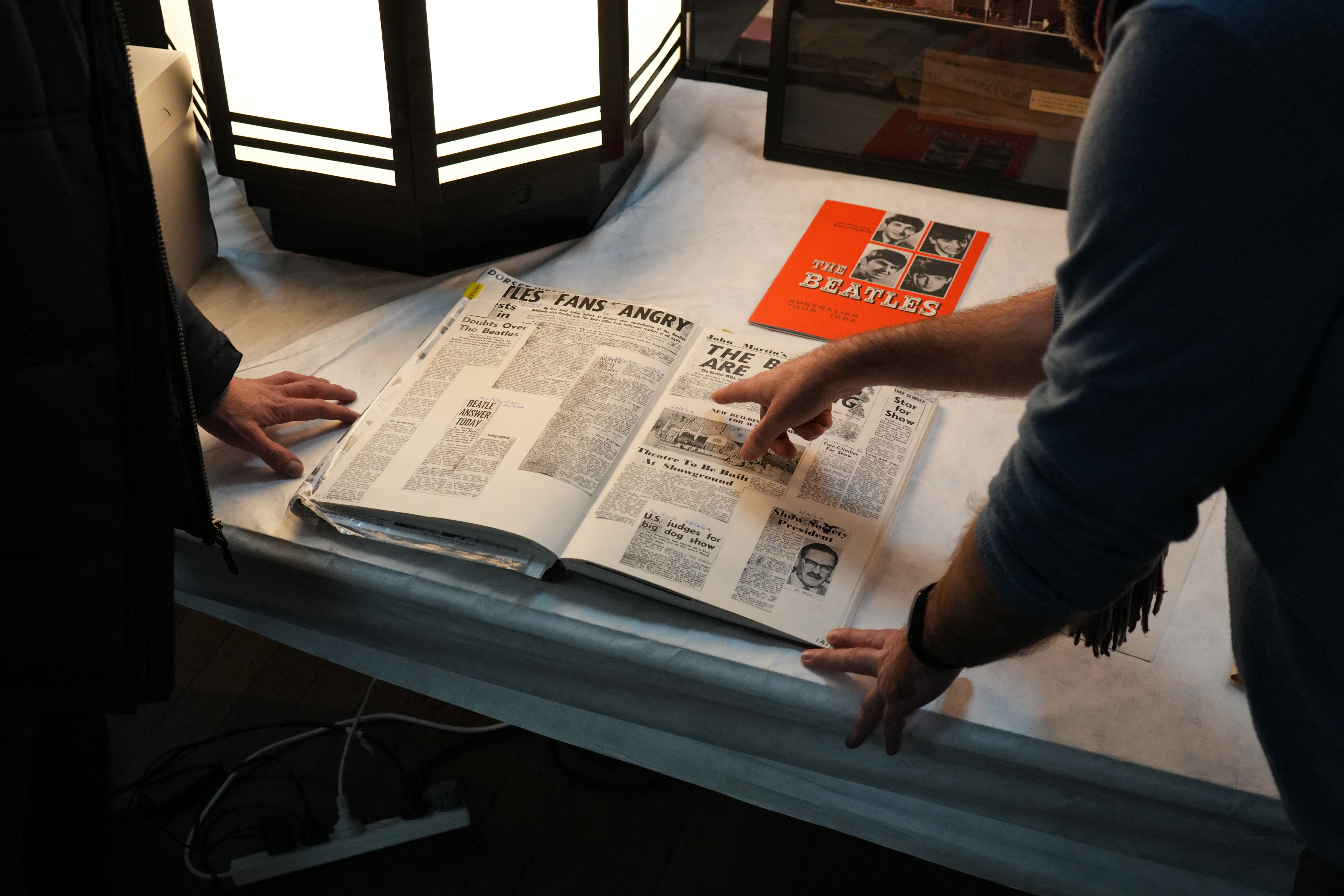 Two people looking at a scrapbook filled with newspaper articles about the Beatles.