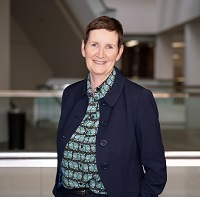 A woman standing in front of a railing with a blue shirt and navy jacket smiling at the camera