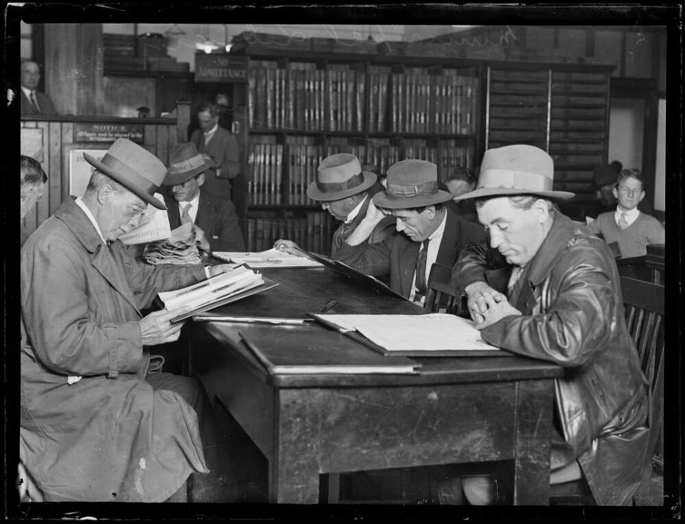 A group of men sit at a table reading