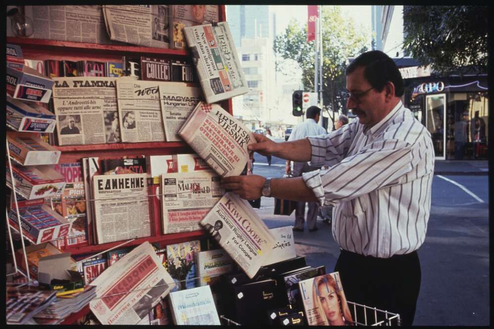 A man stands in front of a newspaper stand