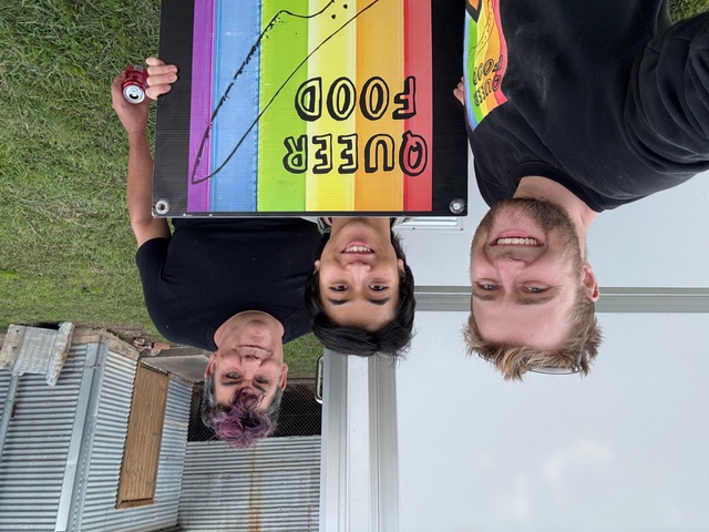 Andy de Groot and other members of the Queer Food team holding their signage