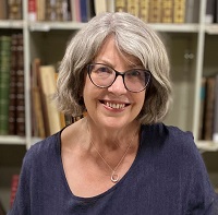 A woman in a purple shirt smiling at the camera and standing in front of a bookshelf.