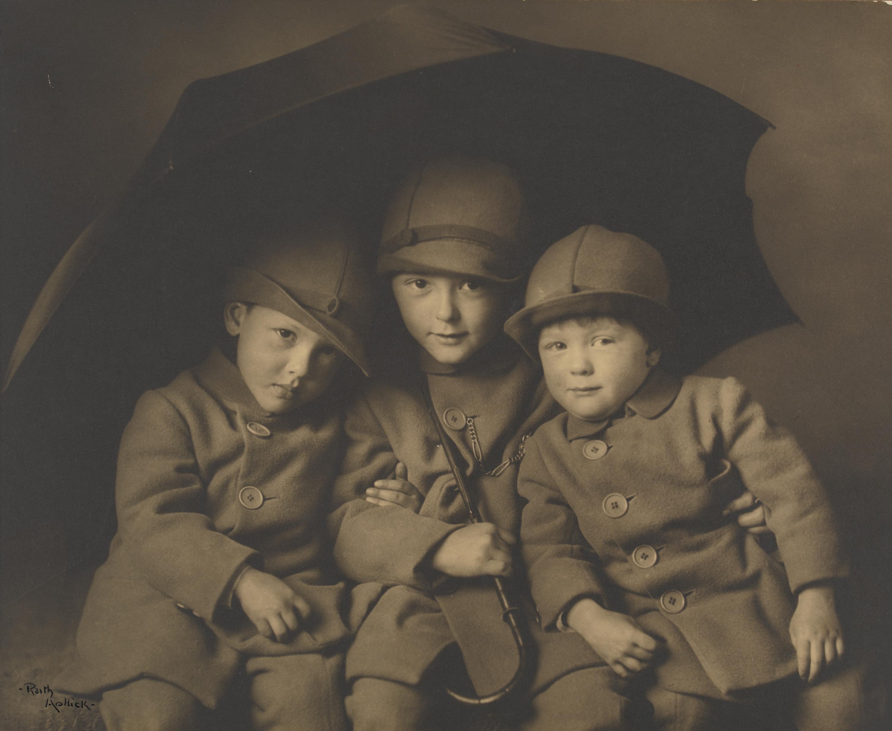 three little boys sitting under a large umbrella