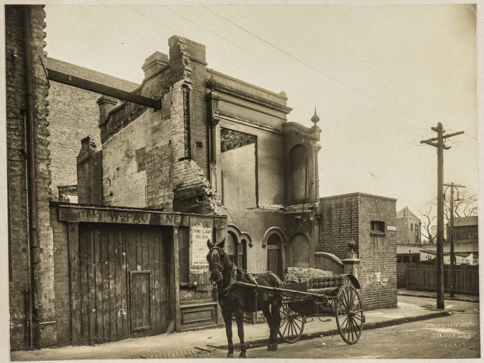 A sepia photo of a half demolished building with a horse and carriage in front of it. 