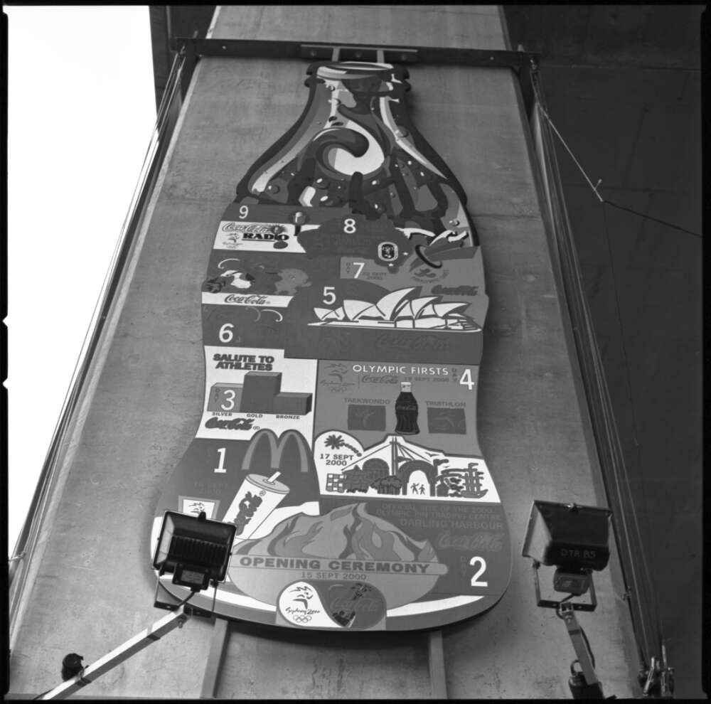 A large sign shaped like a soda bottle. It features illustrations of various components of the Sydney Olympic Games.