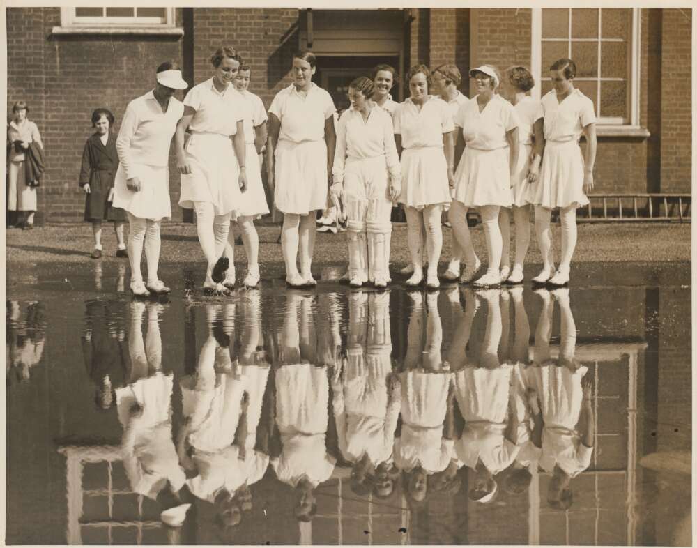 Women's cricket team posed over their reflections in a puddle