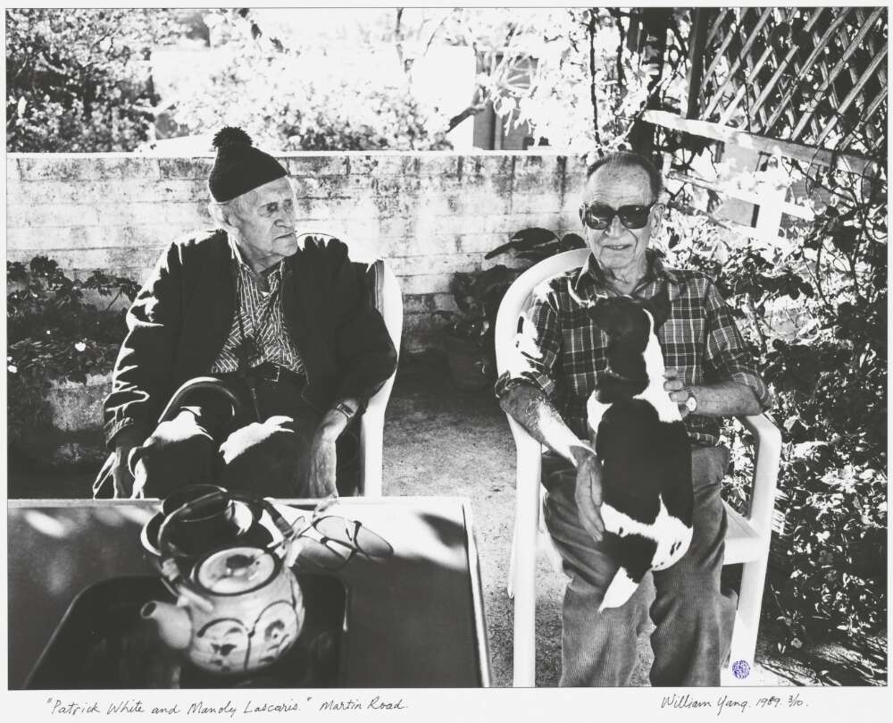Patrick and Manoly sitting an outdoor table. Manoly has a dog on his lap.