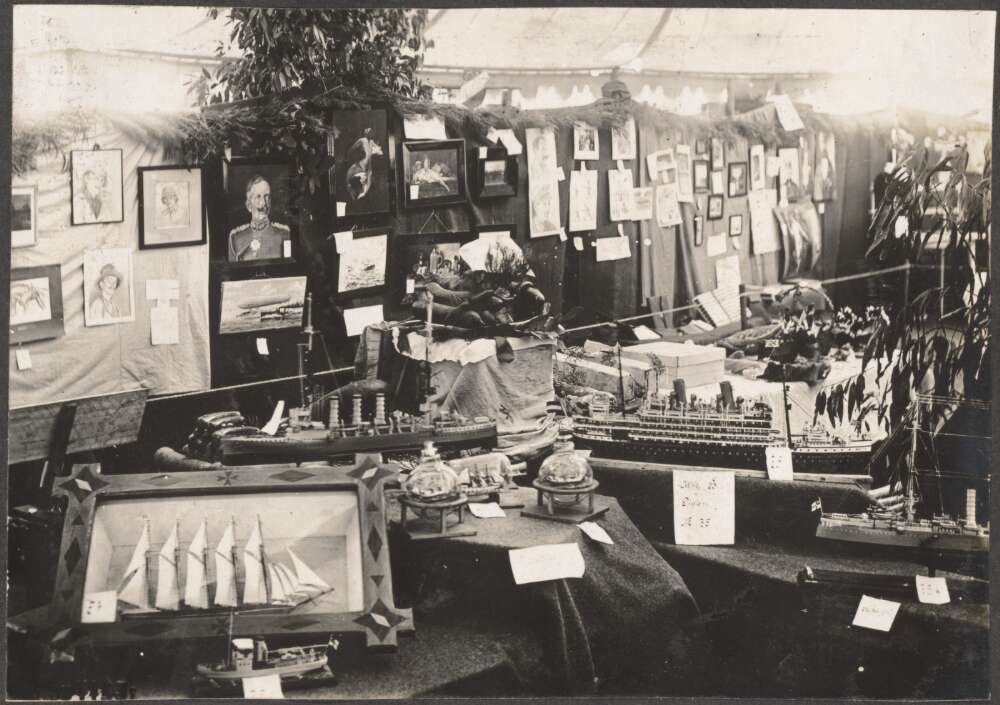 An exhibition with tables full of makeshift items including model ships, drawings and centre pieces. 