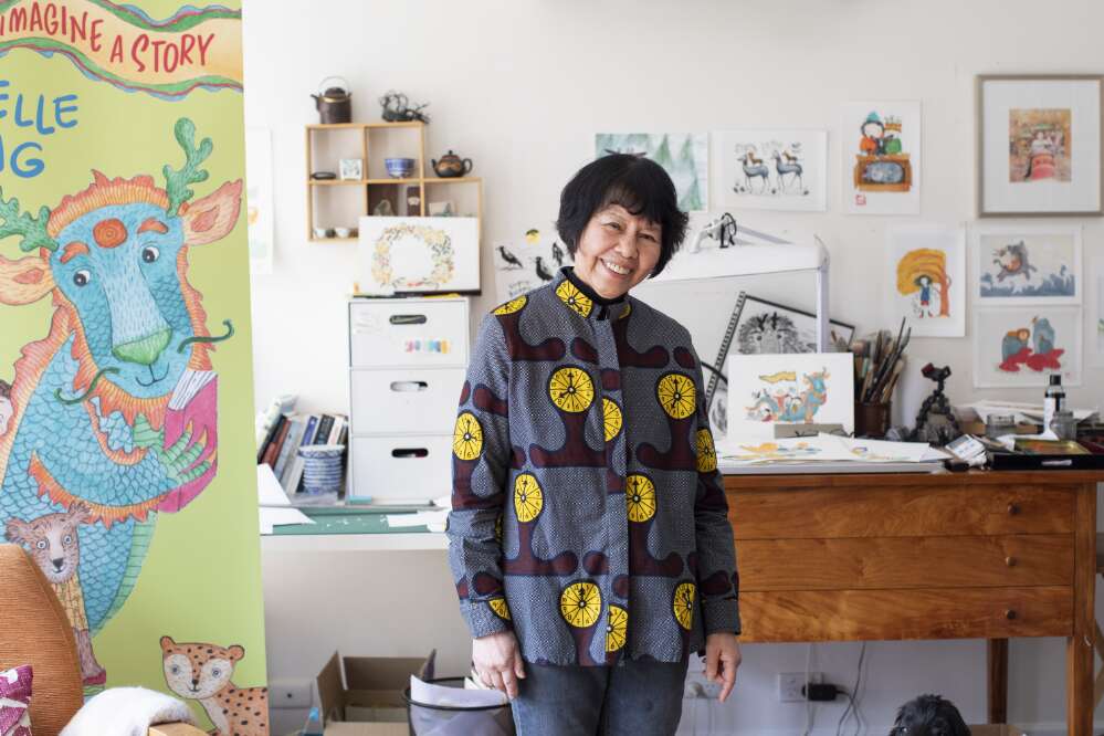 Portrait of Gabrielle Wang standing in her studio in front of a desk, illustrations and children's laureate of the year banner