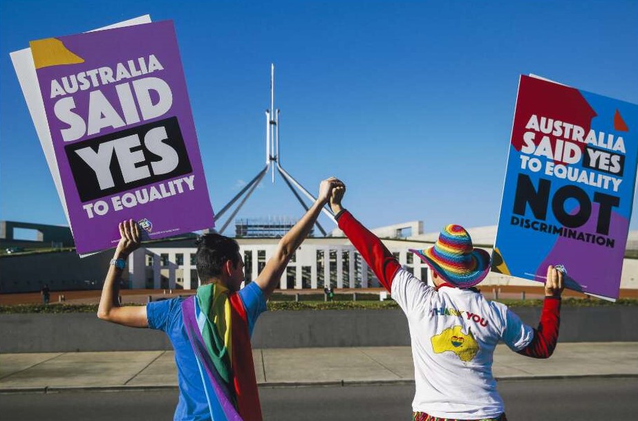 Two people holding hands while raising yes vote marriage equality signs in front of parliament house