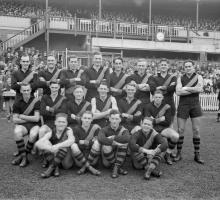 Richmond Football Club in front of a grandstand with fans behind them