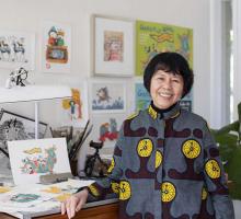 Portrait of Gabrielle Wang standing in her home studio with childrens book illustrations behind her