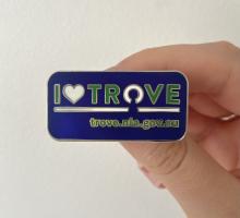 Hand holding a purple 'I heart Trove' badge