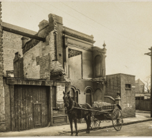 A sepia photo of a half demolished building with a horse and carriage in front of it. 